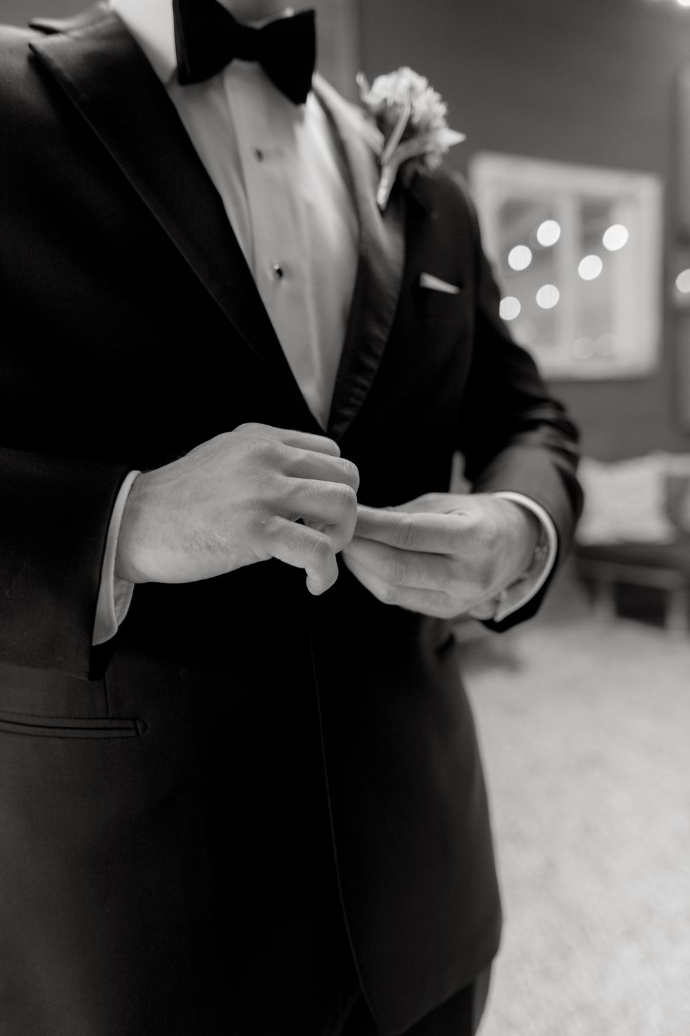 Close-up of a classic black tuxedo with bow tie and boutonniere against a blurred background.