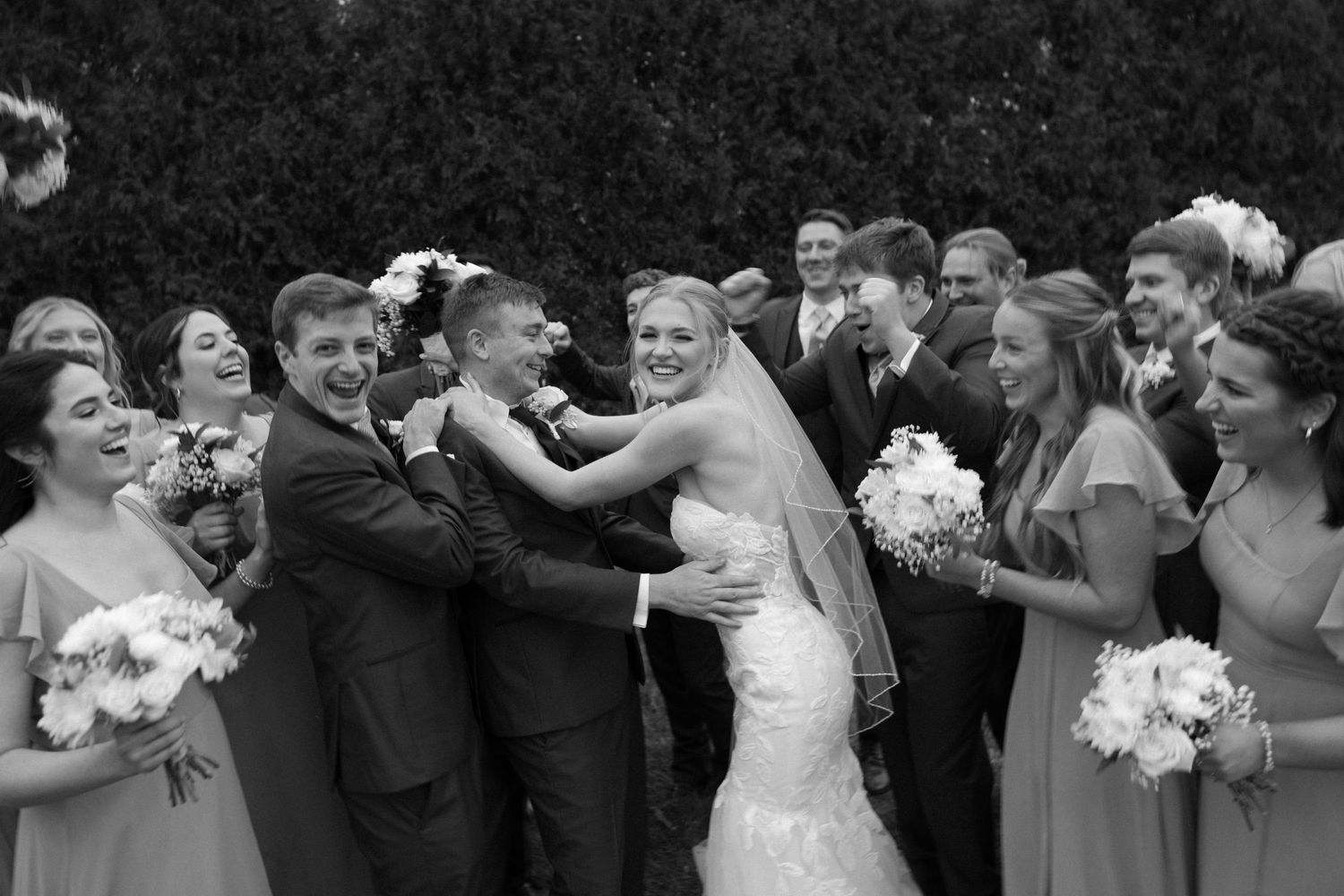 Black and white photo captures joyful wedding party celebration moment.