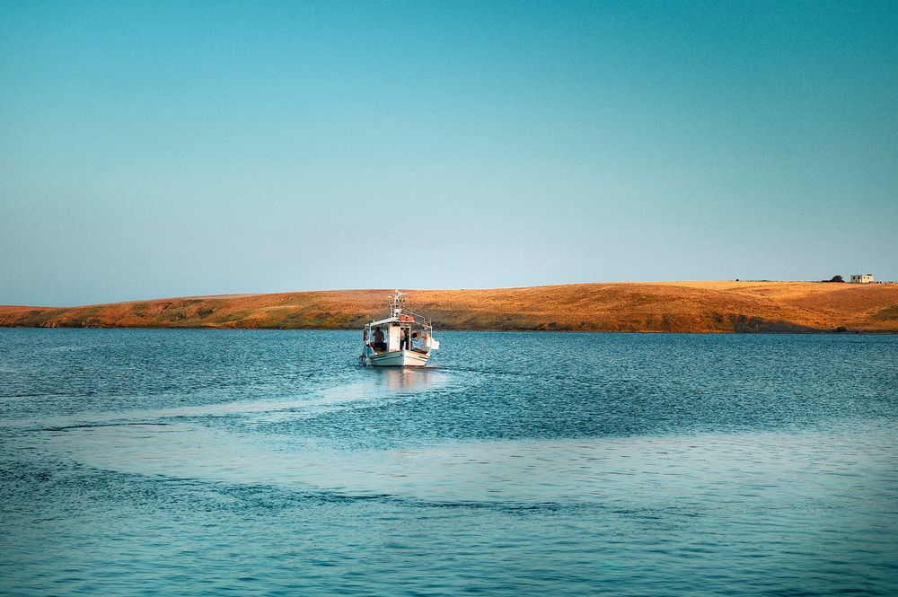 A speedboat cruises across tranquil blue waters with desert cliffs and shoreline visible in the background.