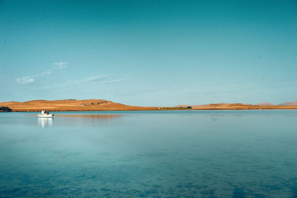 A panoramic view of a tranquil lake with sandy shores and turquoise waters stretching to the horizon.