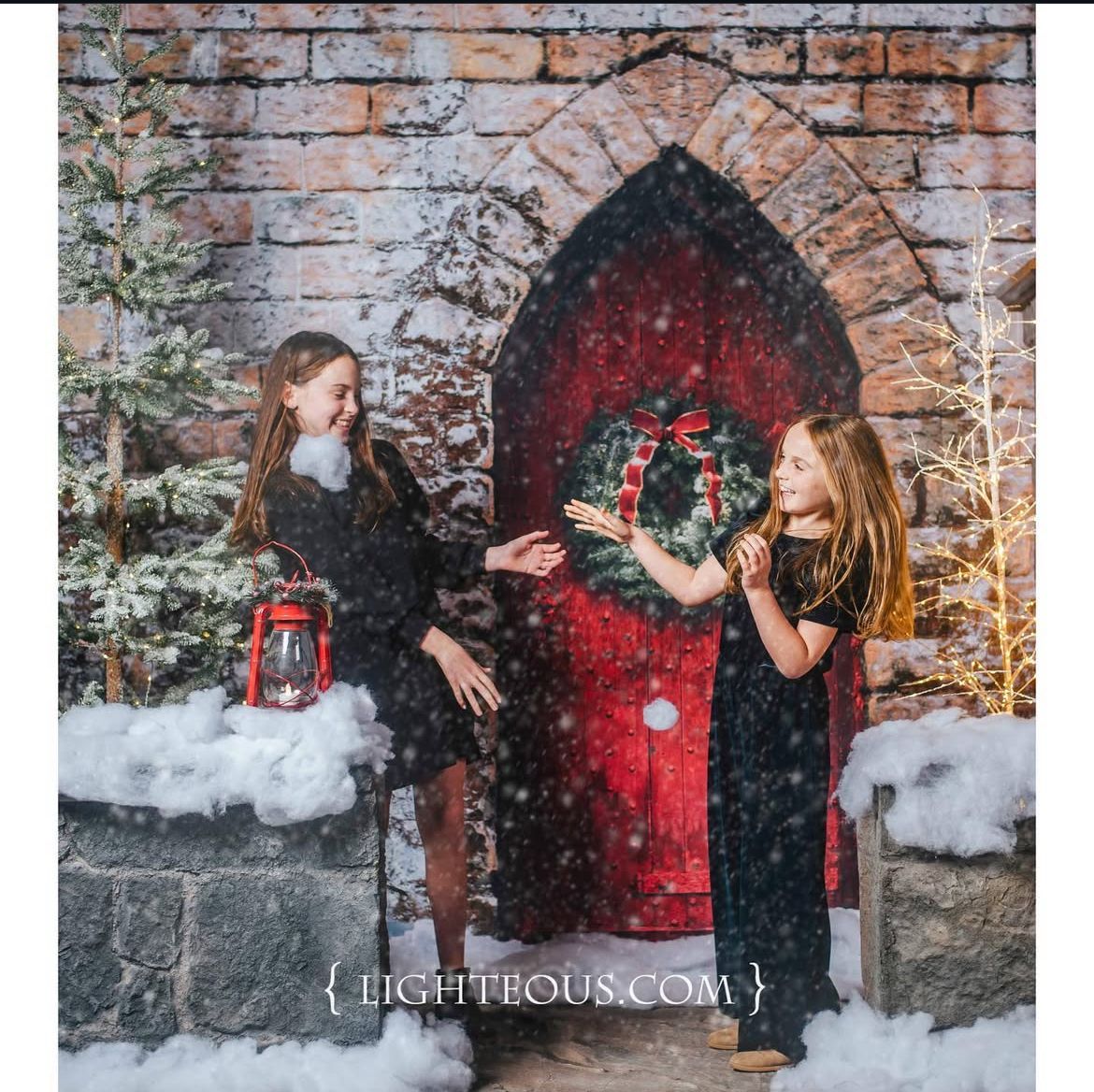 Winter portrait with two people throwing snow in front of red door with wreath.