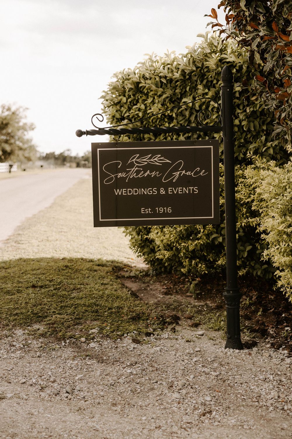 Elegant black wedding venue signage mounted on posts along a landscaped path.