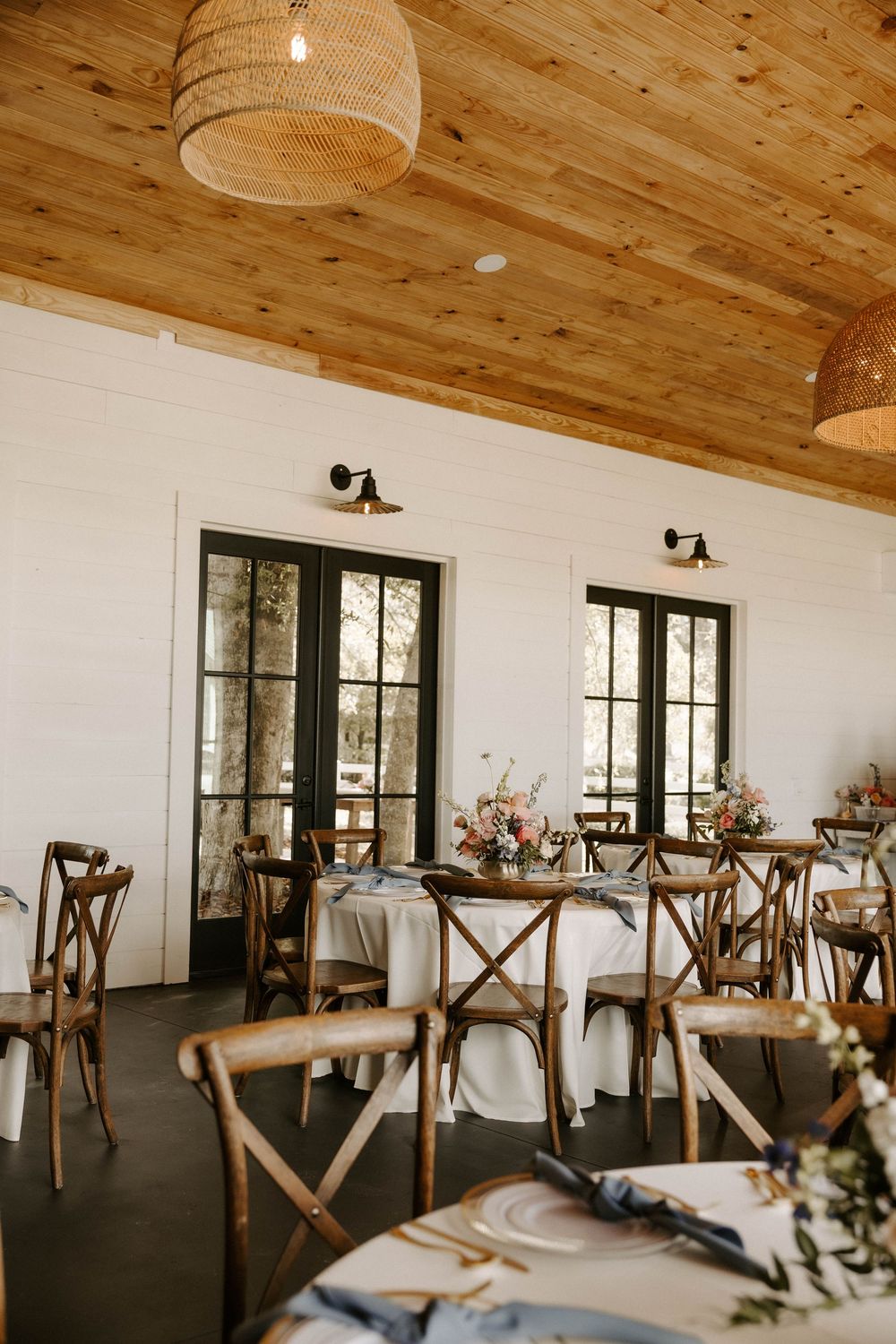 Modern rustic event space interior with wooden ceiling and cross-back chairs.