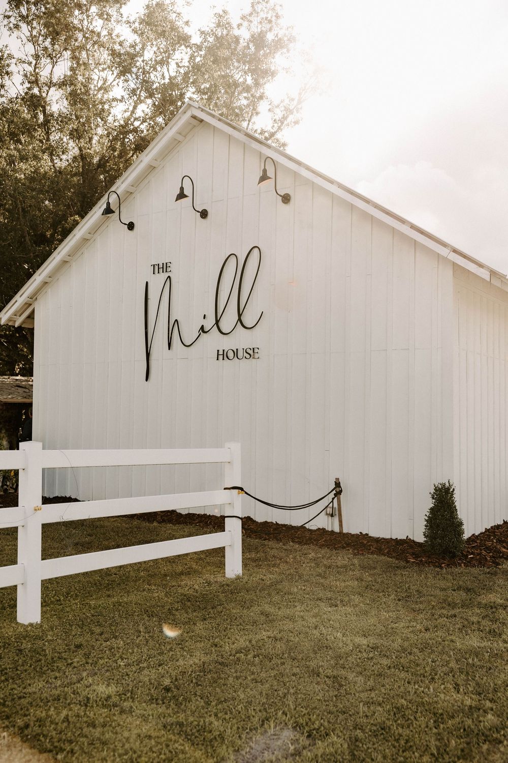 White modern farmhouse venue with 'The Mill House' signage on sloped lawn.