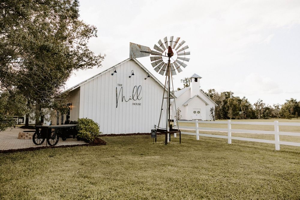 Panoramic view of a white barn wedding venue with windmill against cloudy sky.