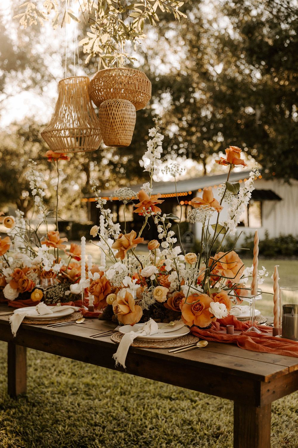 Elegant table setting with peach flowers and woven pendant lights for outdoor reception.