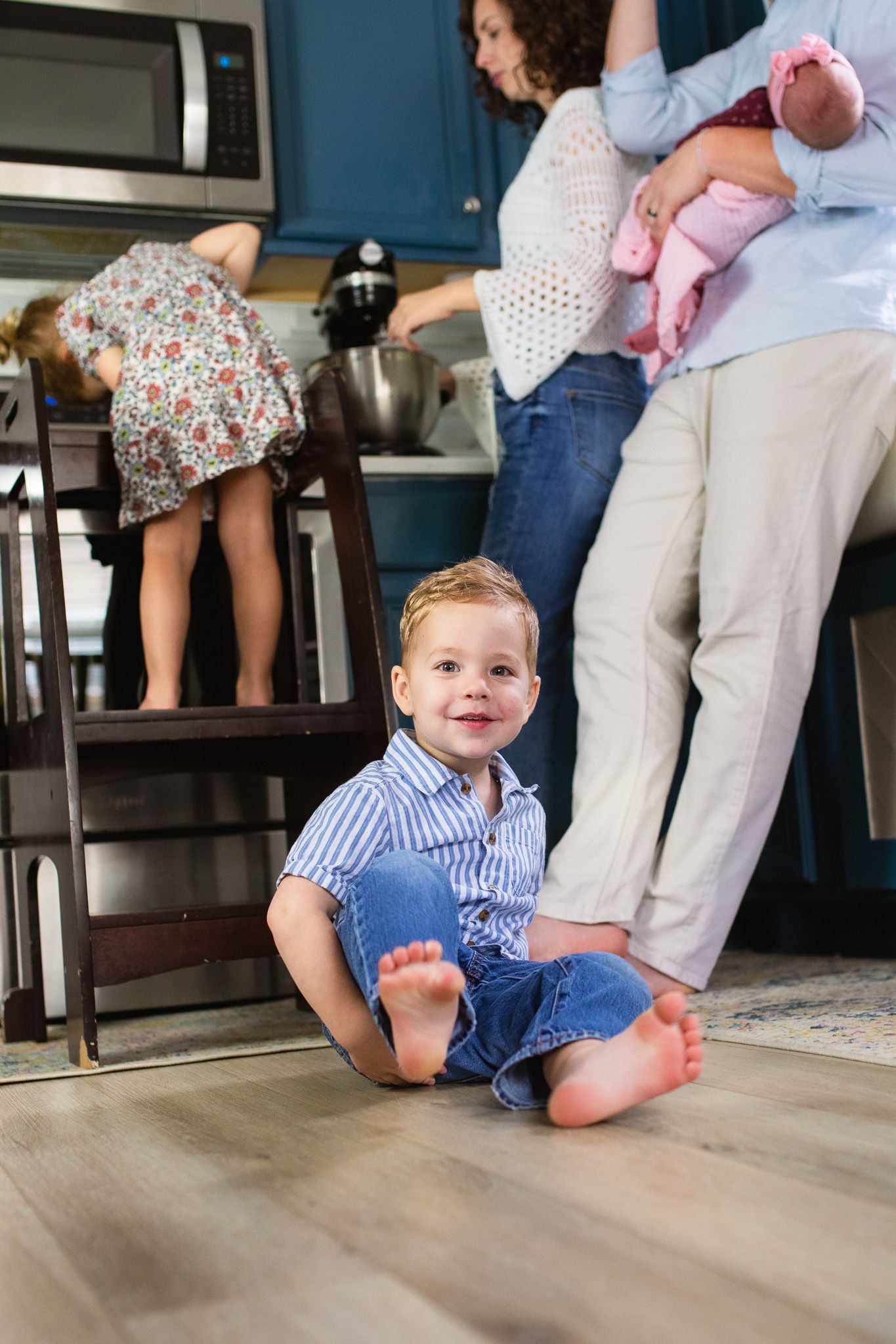 a child in a blue shirt sitting and sliding across a hardwood floor in the kitchen