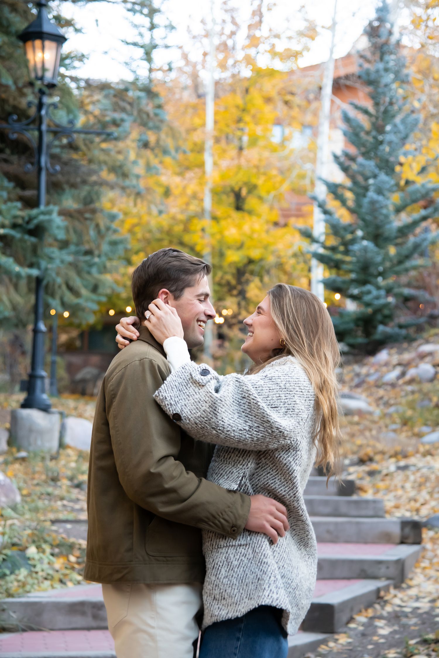 A couple shares a romantic embrace on stone steps surrounded by autumn trees and fallen yellow leaves during a proposal in Vail Village