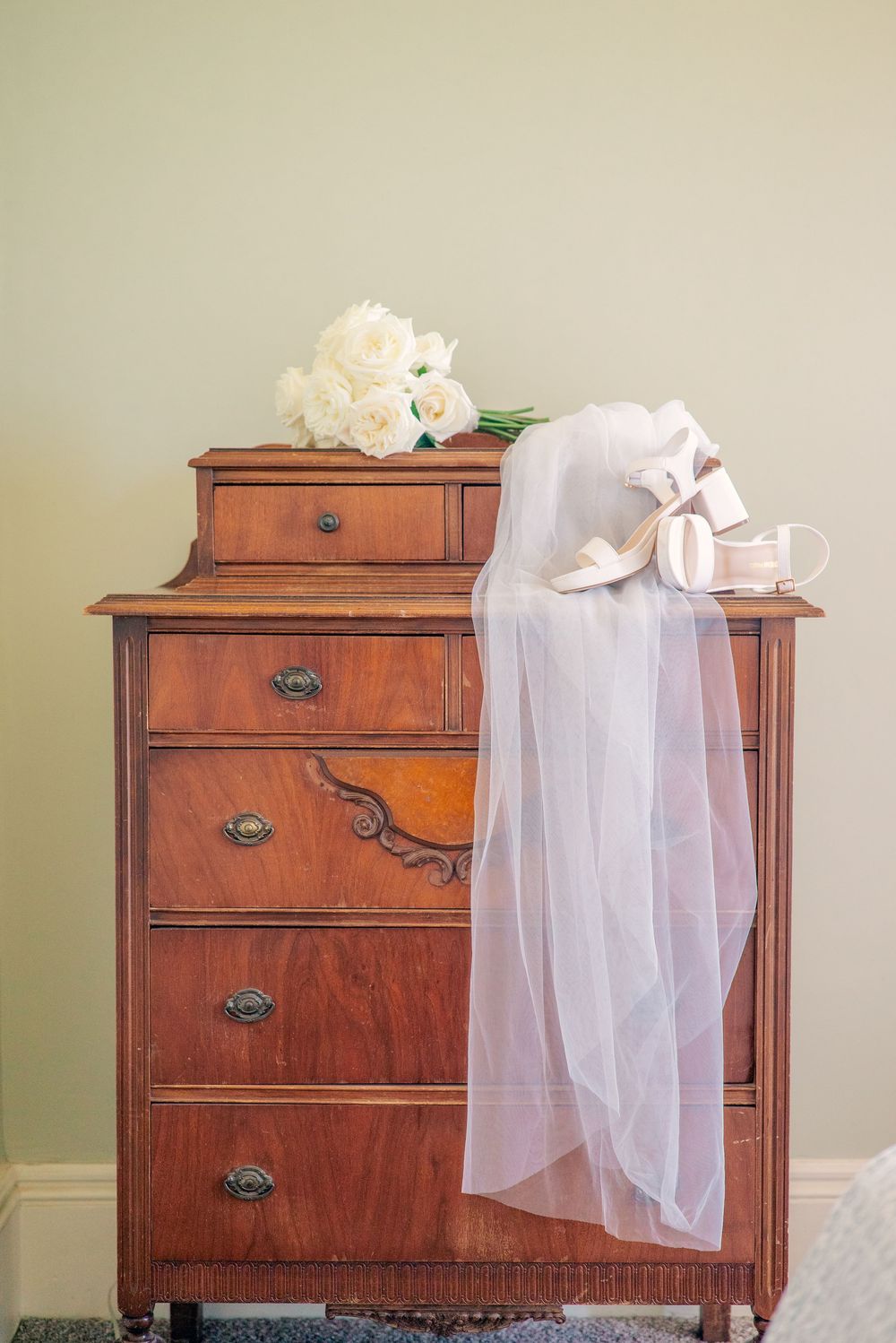 A white veil and floral arrangement rest atop an antique wooden dresser.