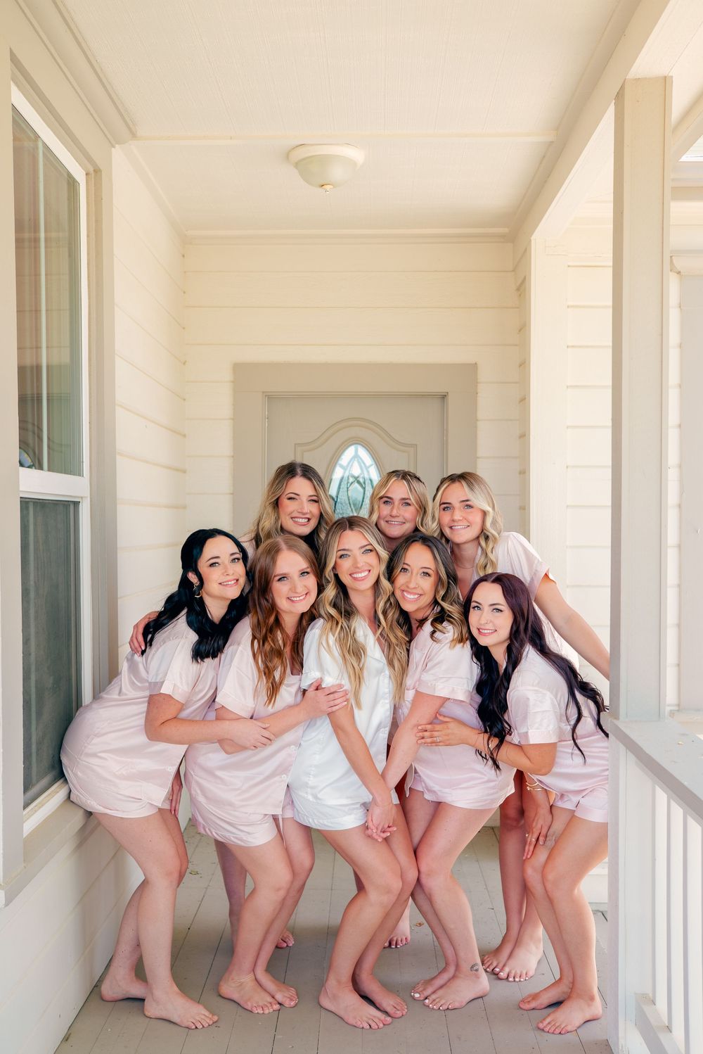 A group poses together wearing matching pink robes on a white porch.