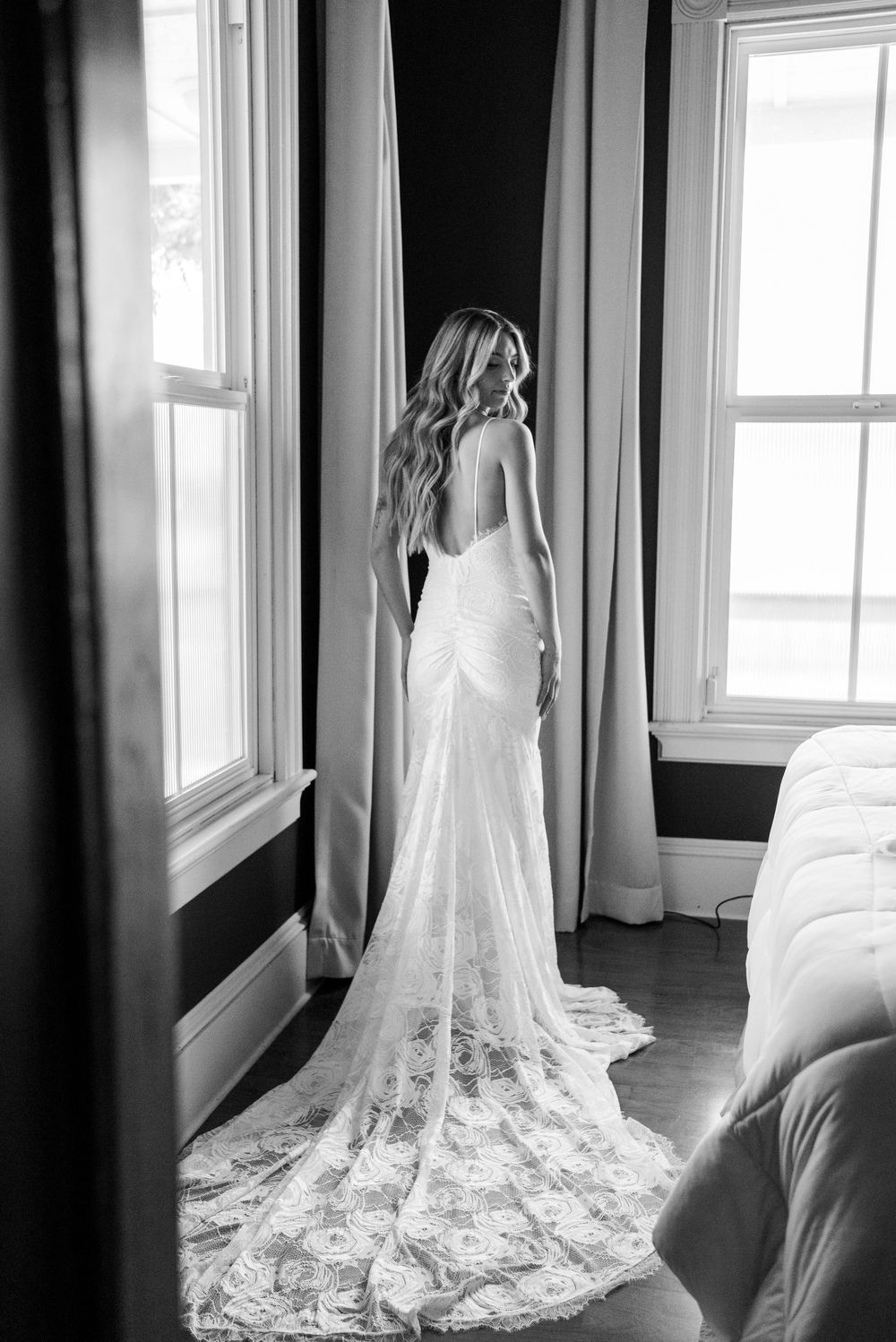 A flowing white lace wedding dress train spreads across a dark hardwood floor.