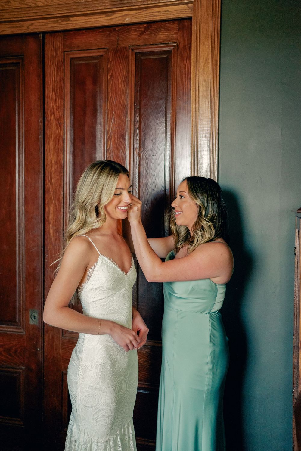 Two people in formal attire share a candid moment against wood-paneled walls.