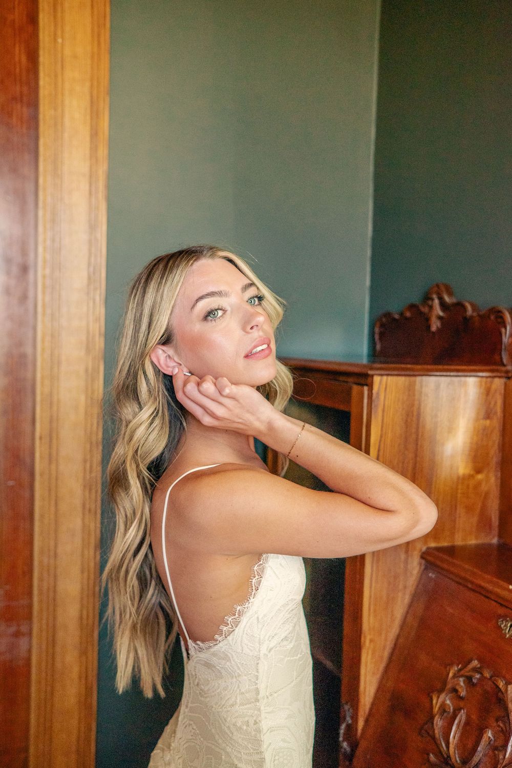 Bride in a white dress puts on earrings while getting ready in an elegant wood-paneled room.