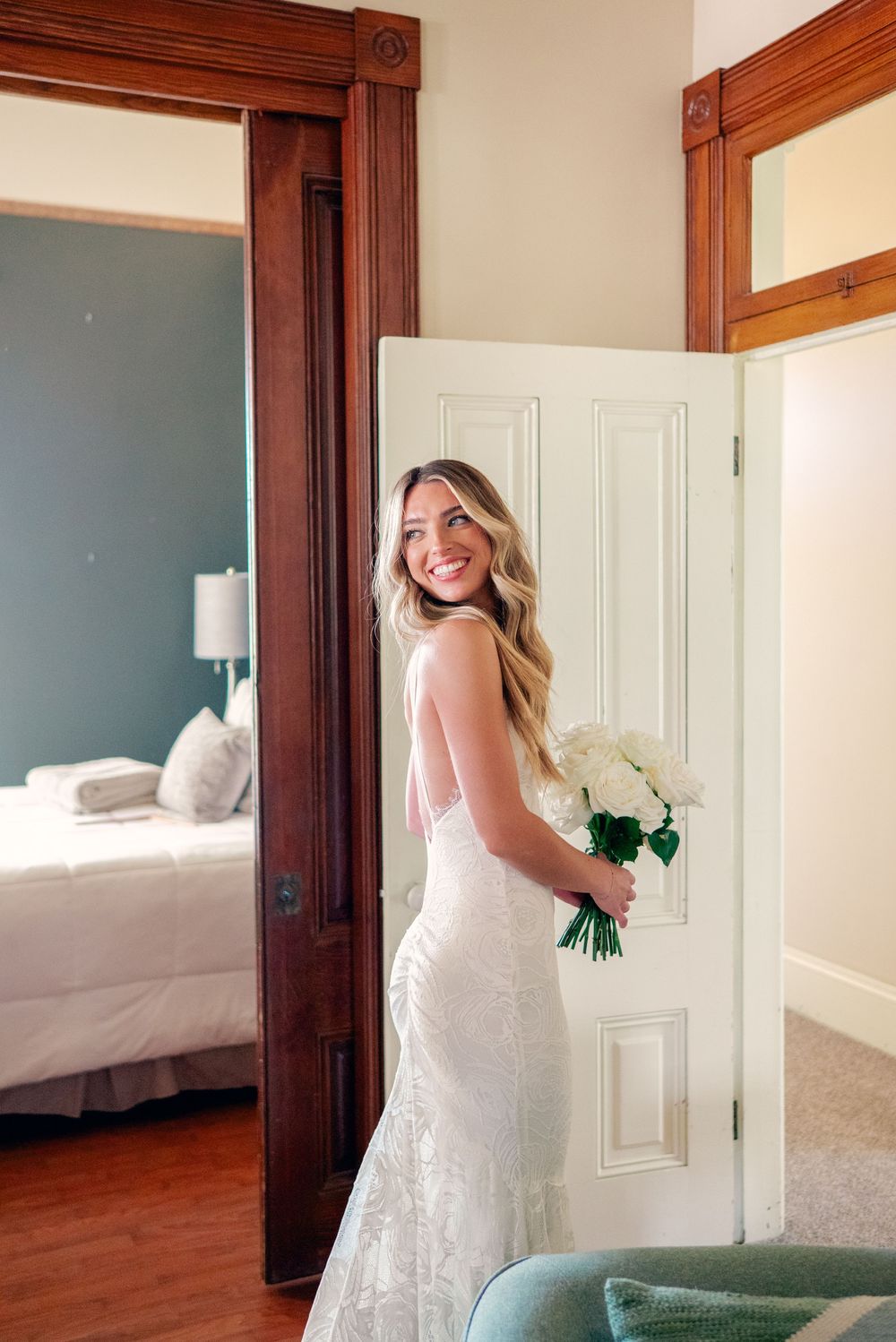 Bride in fitted lace wedding dress poses in a room with dark wood trim and white walls.