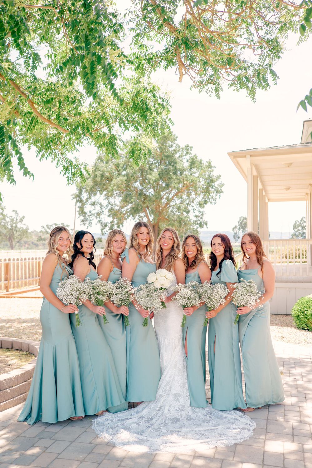 Bridal party in matching seafoam blue dresses poses together on a sunny patio.