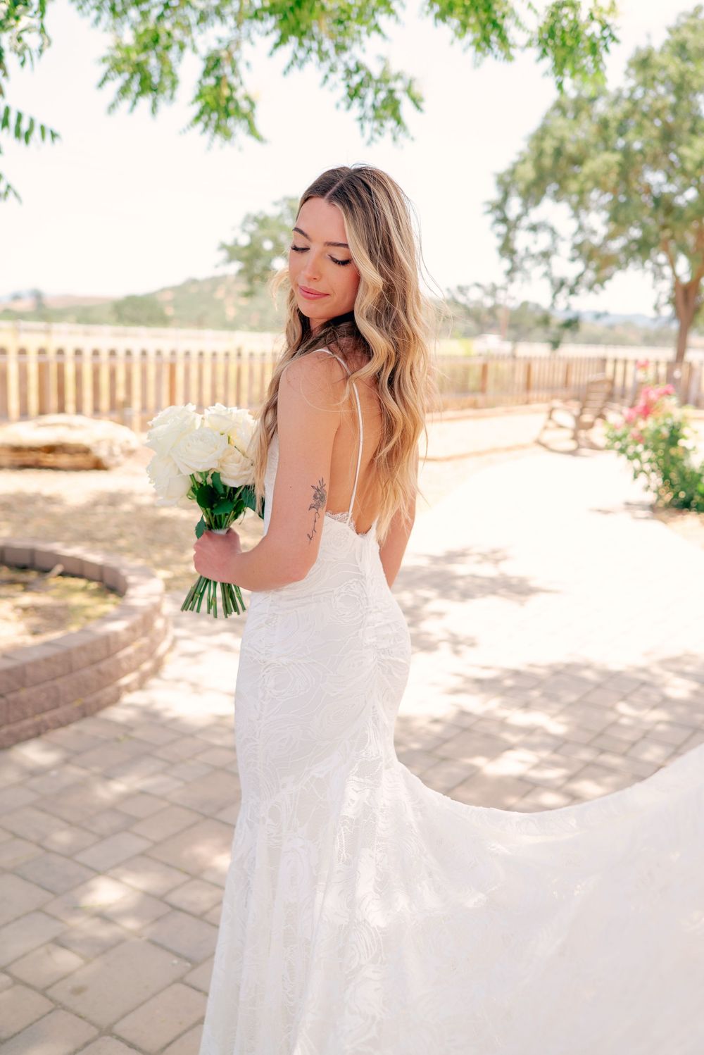 Bride in white lace gown twirls on a sunny stone patio.