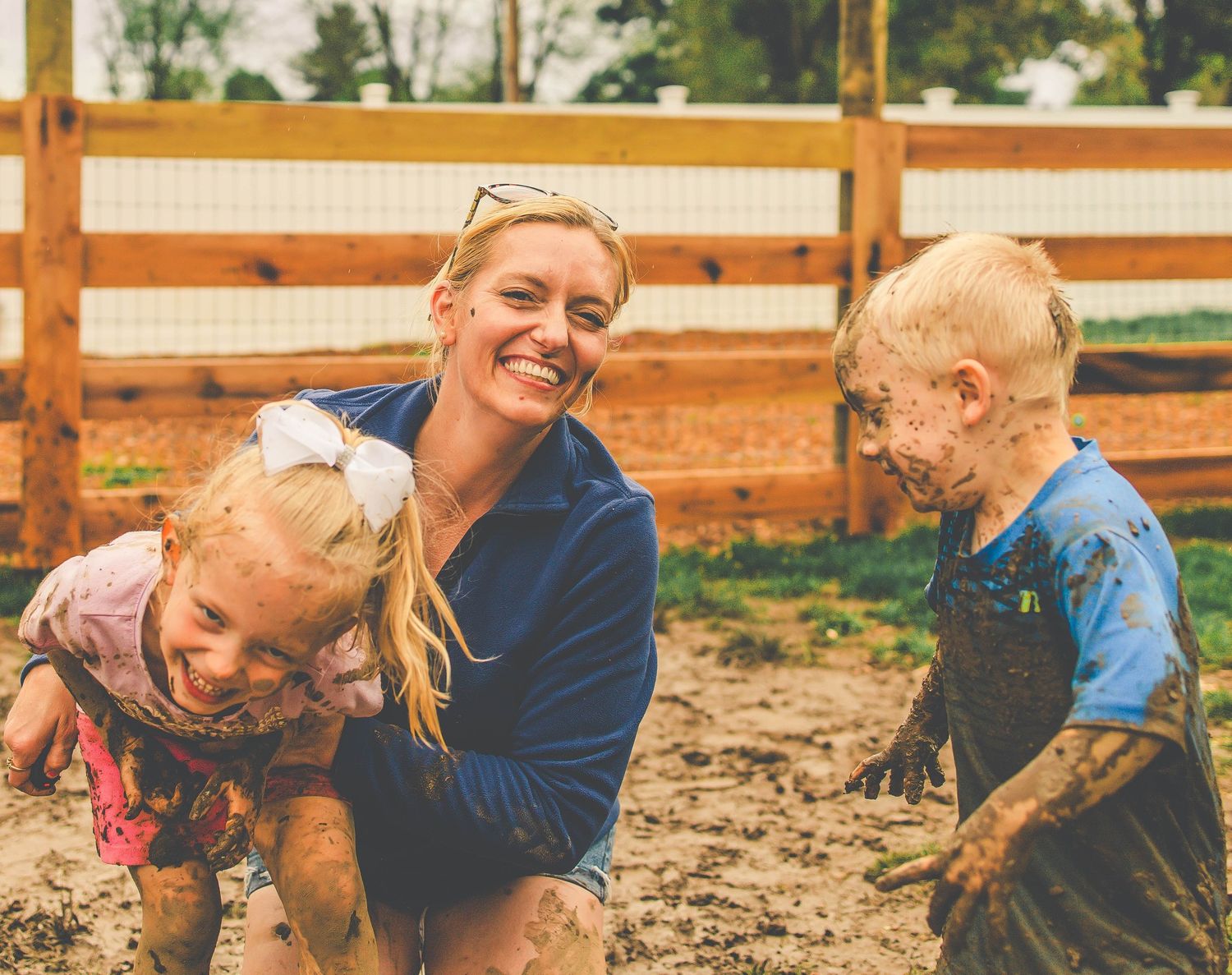 A group of people in blue shirts play and laugh together in muddy soil during an outdoor activity.