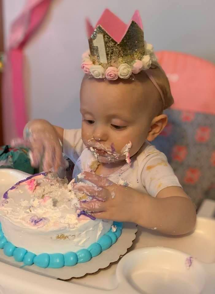 Baby in white outfit smashes into birthday cake with blue frosting border during first birthday cake smash photoshoot.