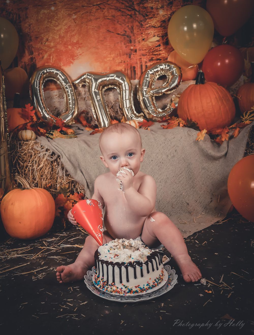 Baby's first birthday cake smash photography session with orange pumpkins and fall-themed decorations.
