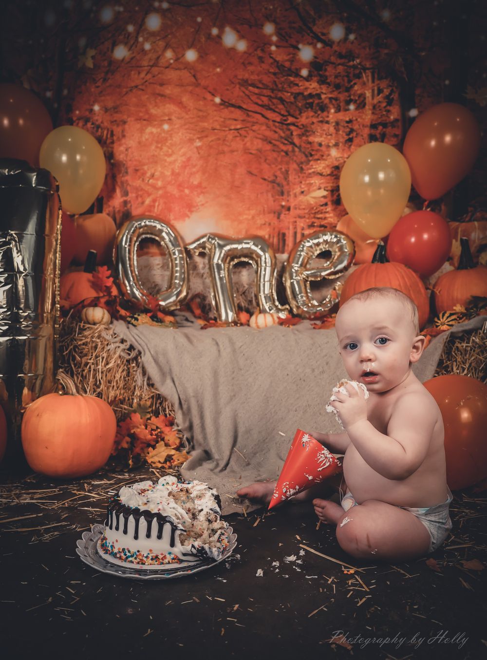 Baby's first cake smash photo session with orange pumpkins and fall decor in rustic setting.