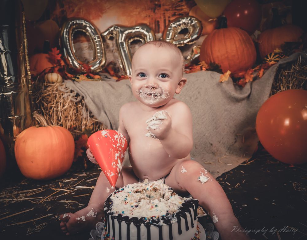 A cake smash photography setup featuring orange pumpkins, rustic decor, and autumn-themed decorations.