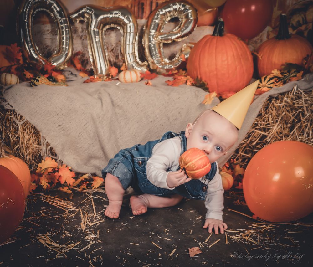 Baby crawling among autumn pumpkins and hay during festive photoshoot.