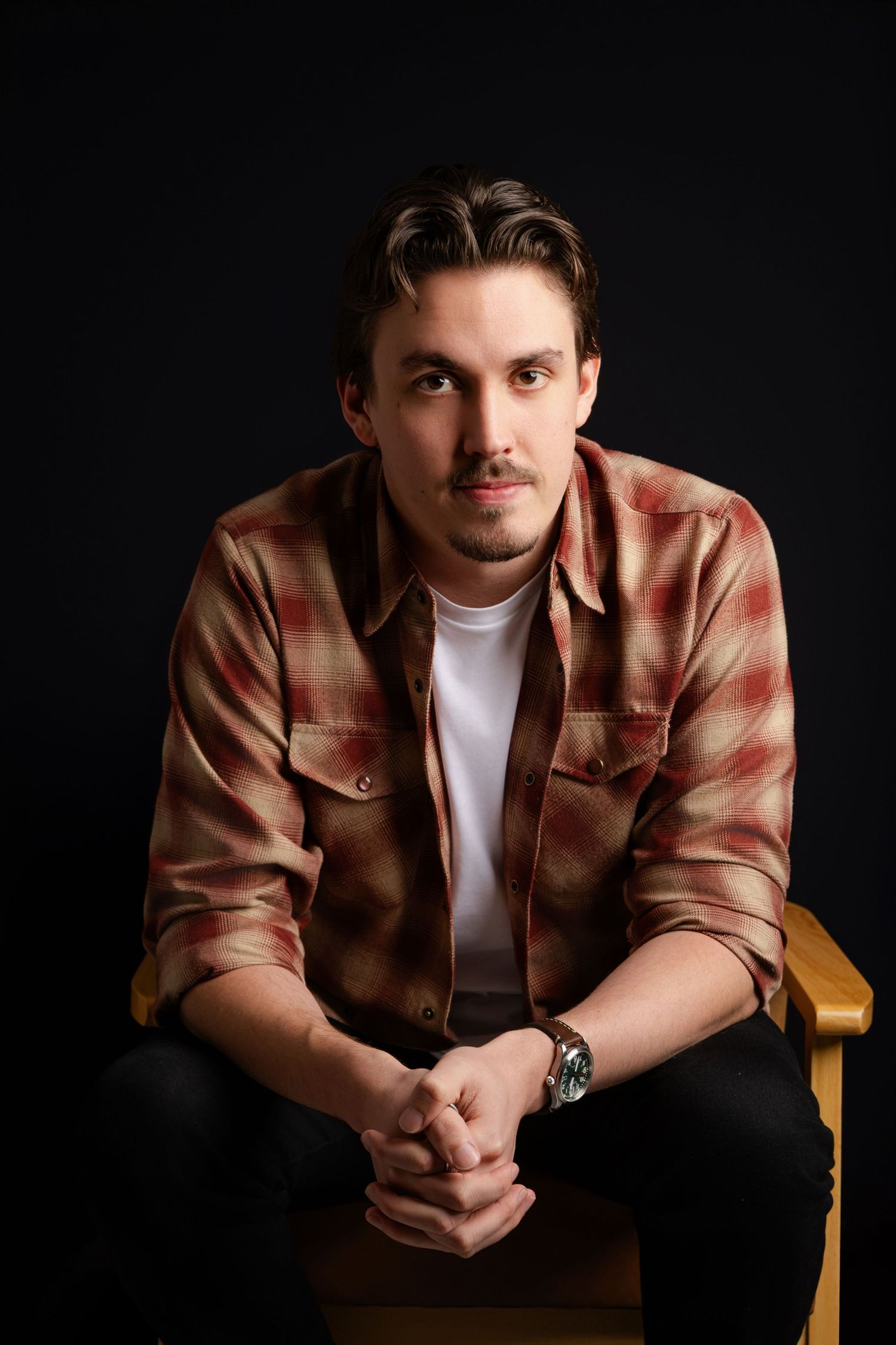 Portrait series in dark studio showing person wearing brown plaid shirt and white t-shirt in various seated poses.
