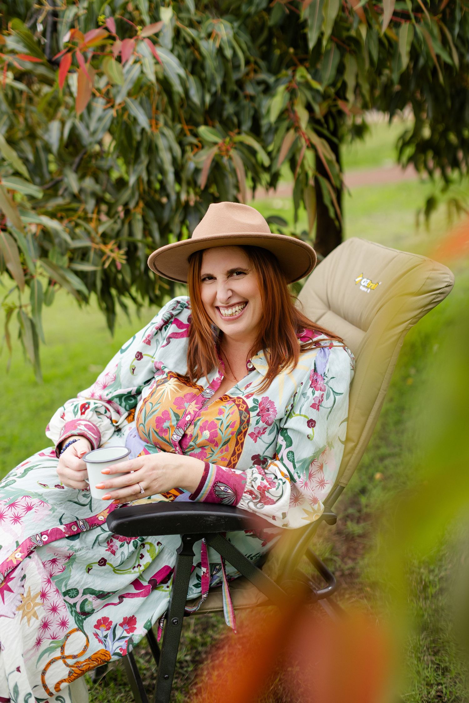 A person in a floral dress relaxes on an outdoor chaise lounge chair surrounded by lush garden foliage.