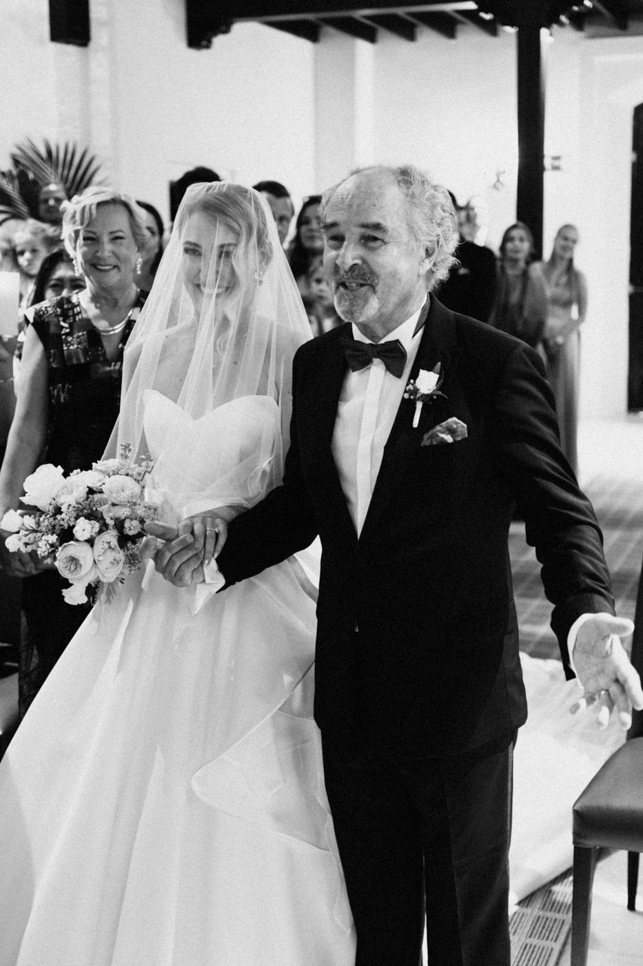 Black and white wedding photo capturing a joyful moment during a bridal procession down the aisle.