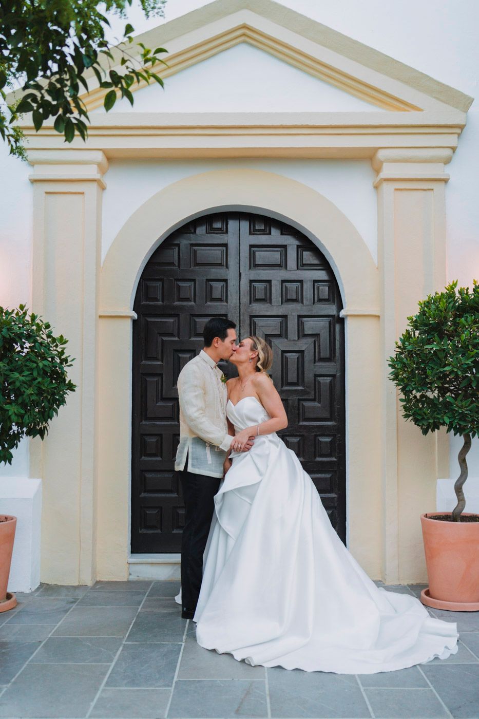 A romantic wedding portrait in front of an elegant cream archway with a dramatic black wooden door.