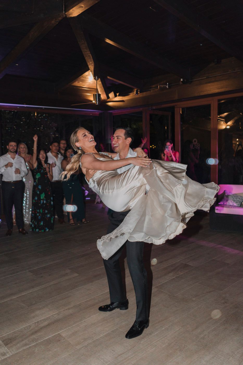 A couple performs a romantic dance move during a reception as the person in white dress is gracefully dipped on the dance floor.