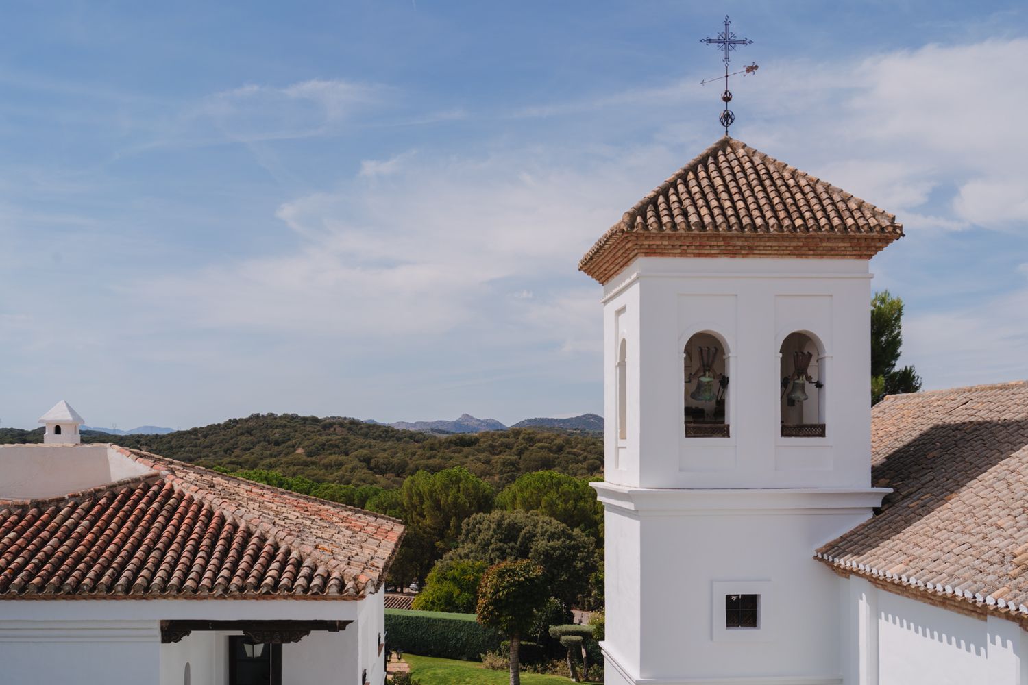 White church bell tower with terracotta roof tiles overlooking rolling hills in Spanish countryside.