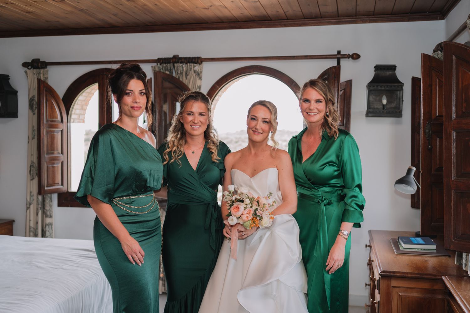 Bridal party poses together in emerald green satin dresses during an elegant Mediterranean wedding celebration.