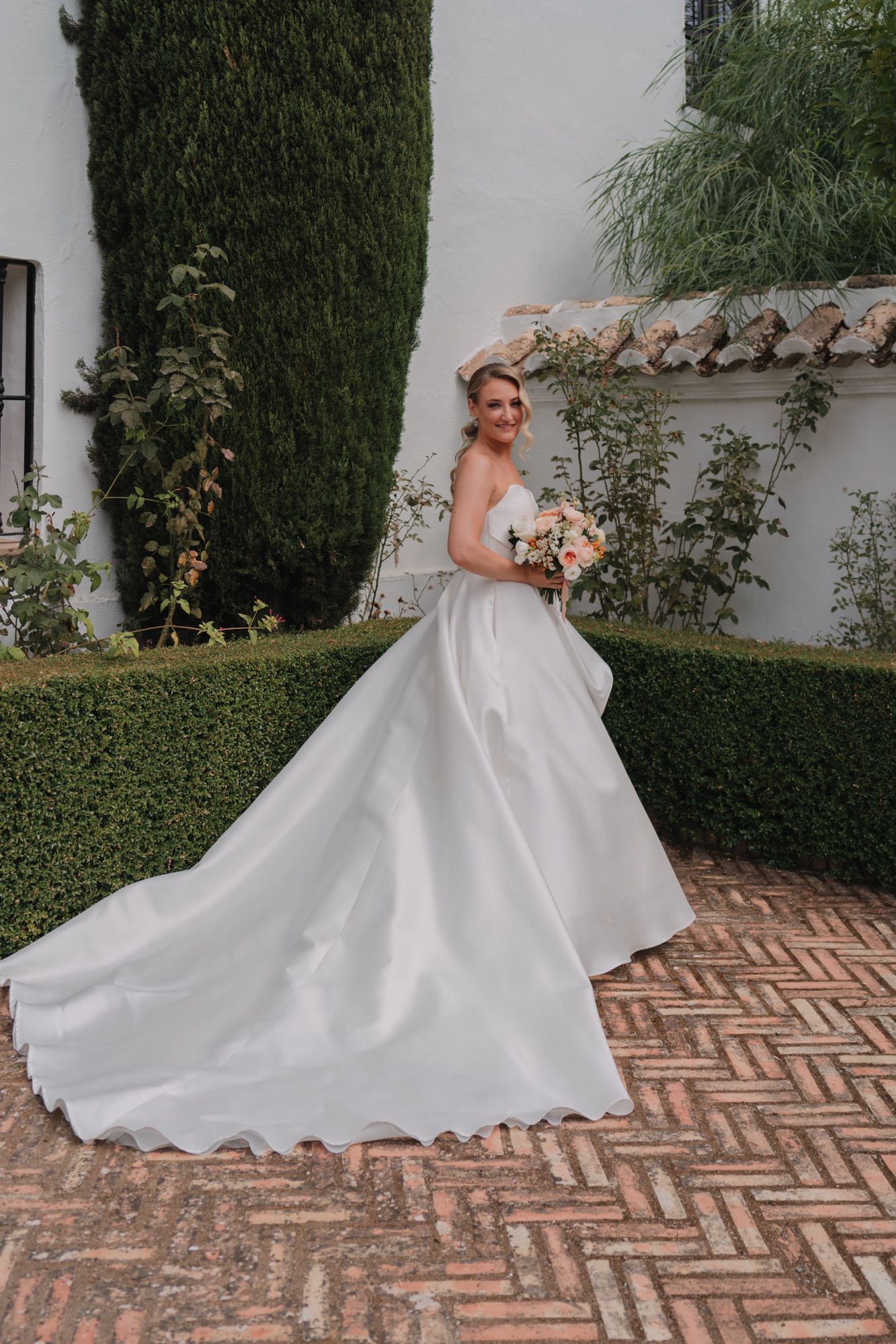 An elegant white wedding gown with dramatic train captured in a Mediterranean-style courtyard setting.