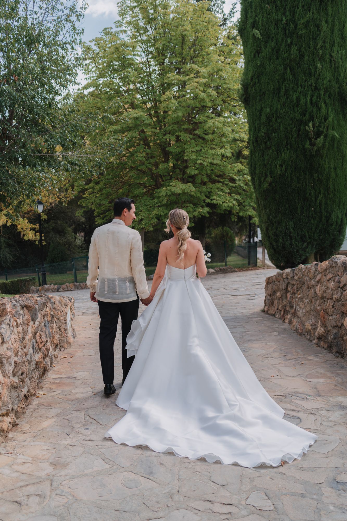 A couple walking together on a stone path surrounded by lush trees and greenery on their wedding day.