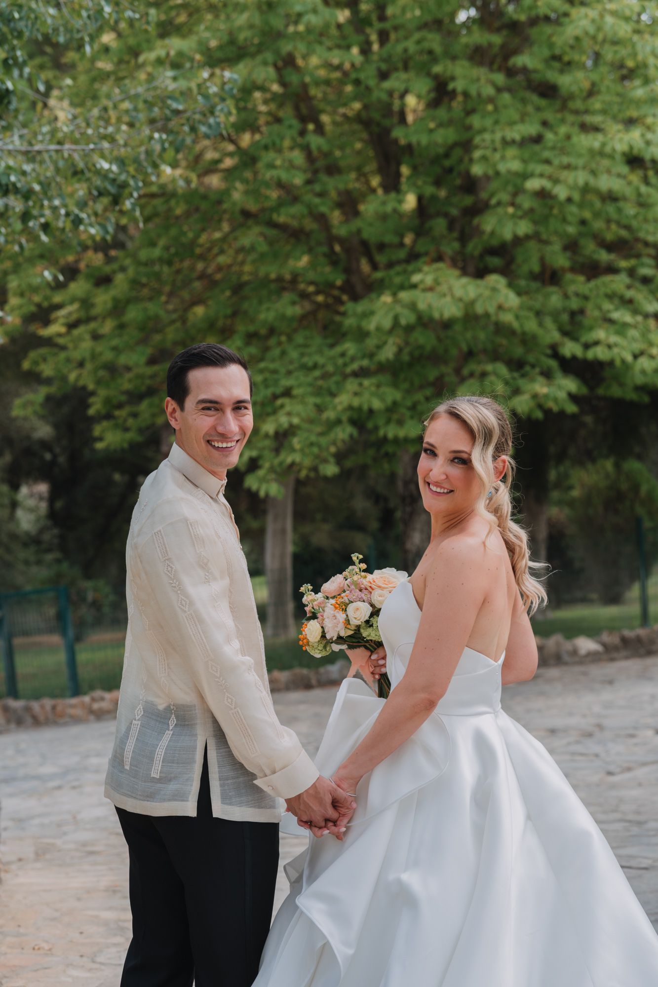 Newlyweds share a joyful moment outdoors with bride in white ballgown holding a bouquet.