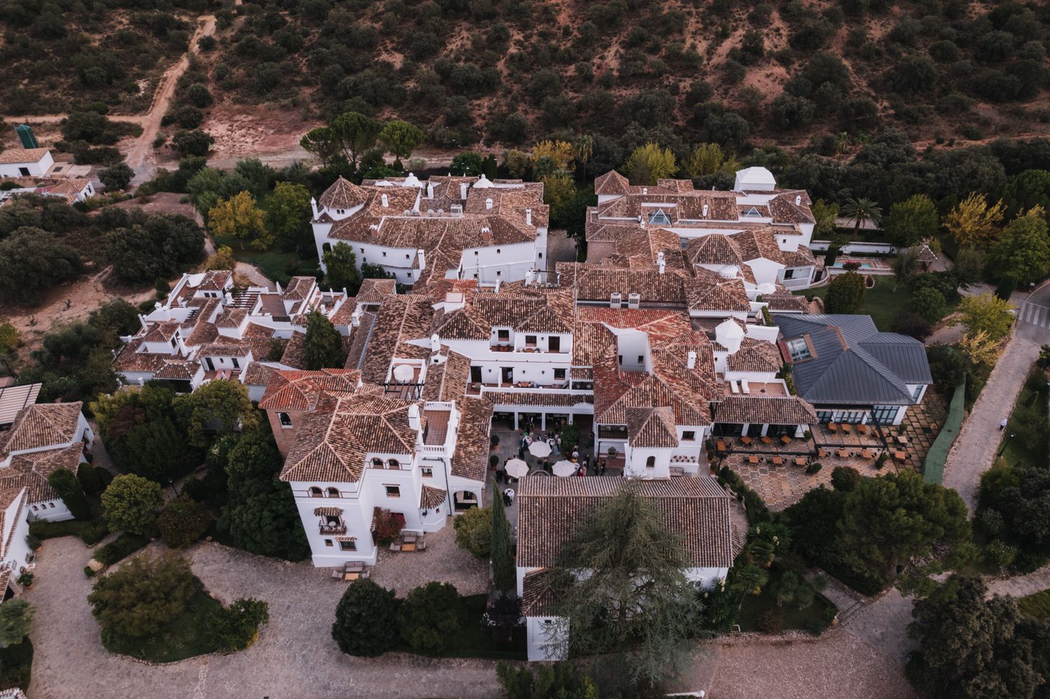 Aerial view of a rustic Spanish village with traditional terracotta roofs and white buildings nestled in hills.