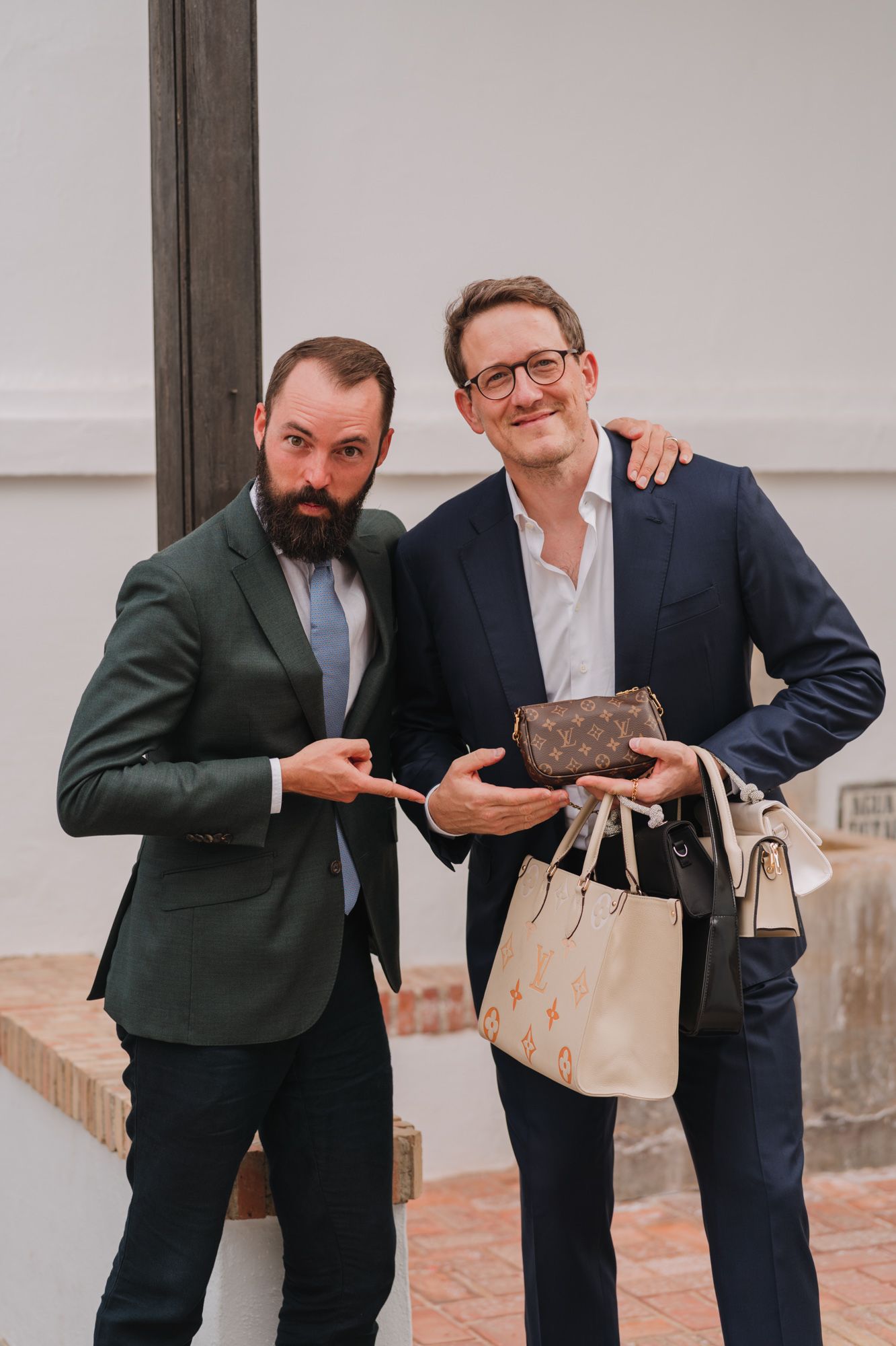 Two guests in formal attire pose together at wedding reception holding accessories.