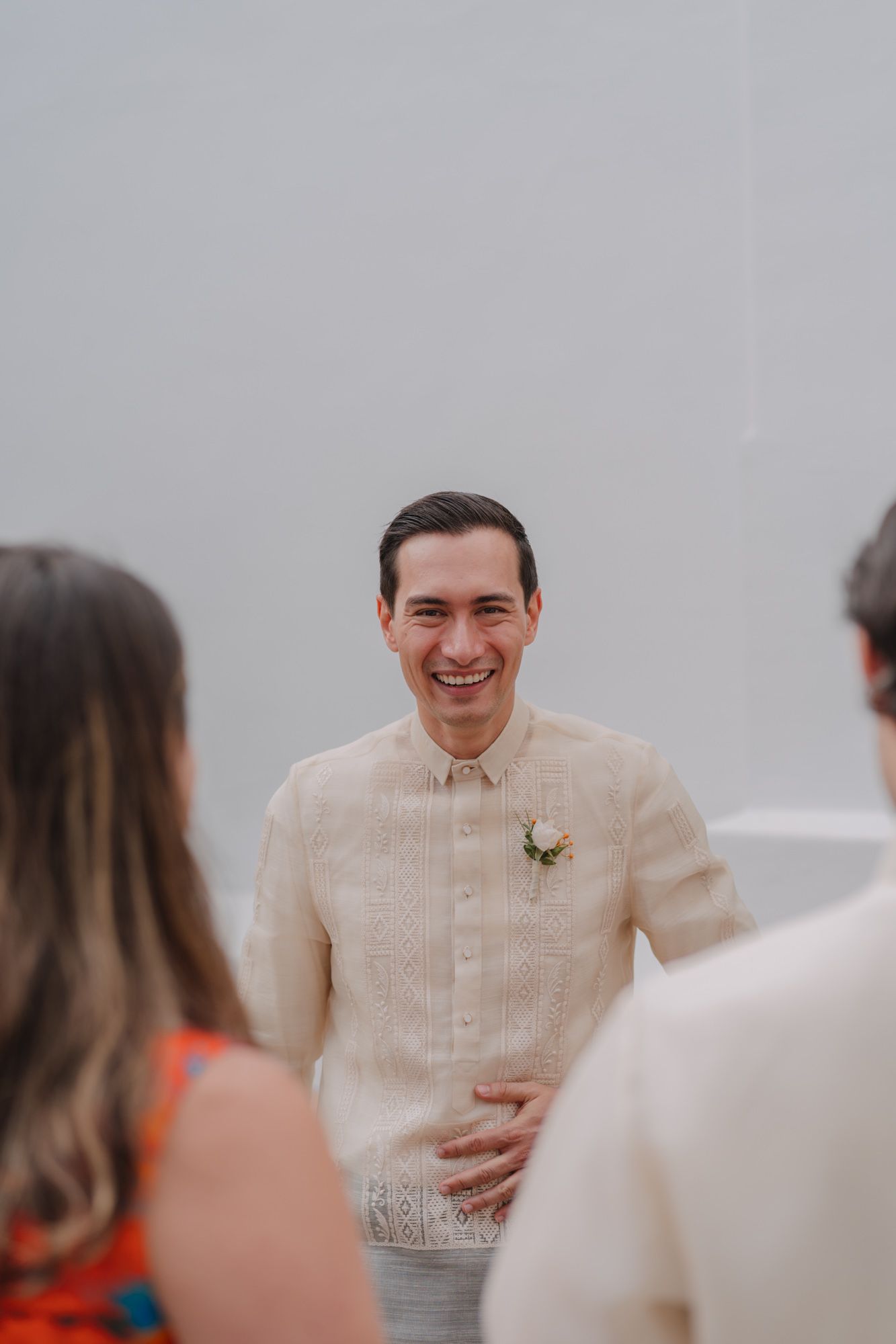 Guest in cream colored formal attire smiling during outdoor wedding celebration.