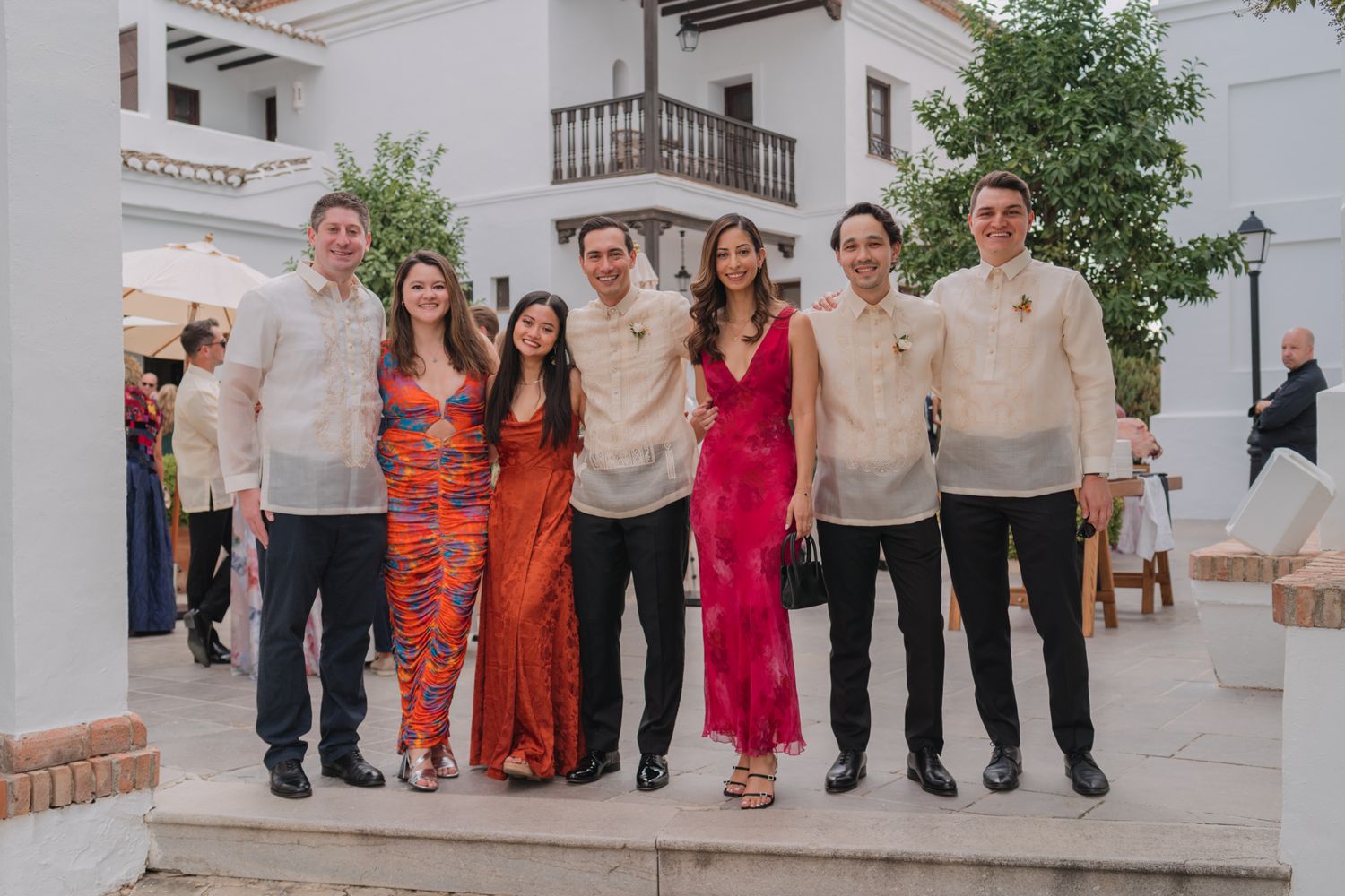A group stands together at an outdoor event wearing formal attire in orange, red, and neutral colors.