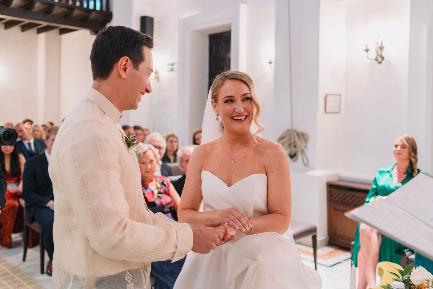 A candid moment during a wedding ceremony shows a couple exchanging rings in a bright indoor venue.