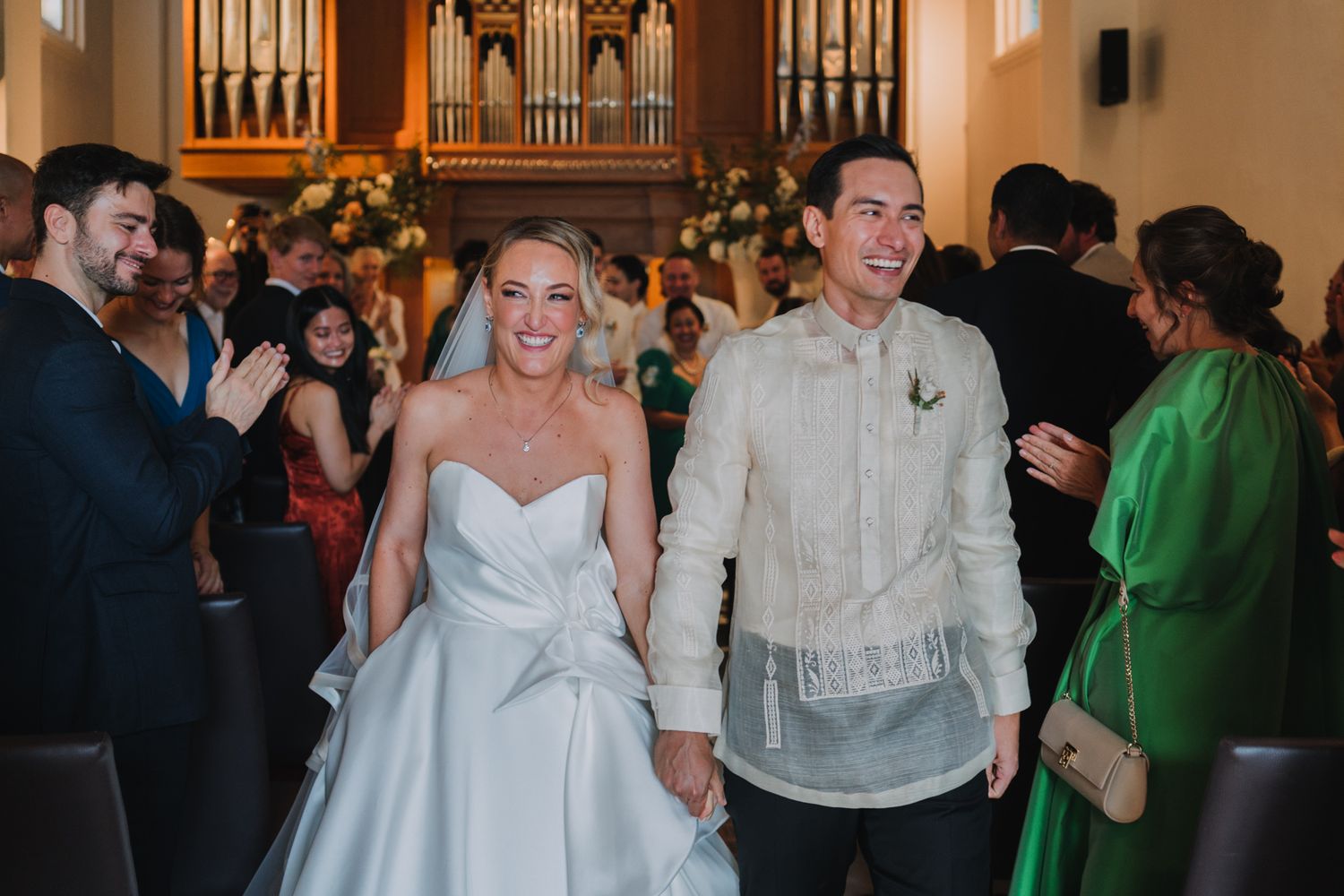 A bride in white and groom in traditional barong exit their wedding ceremony.
