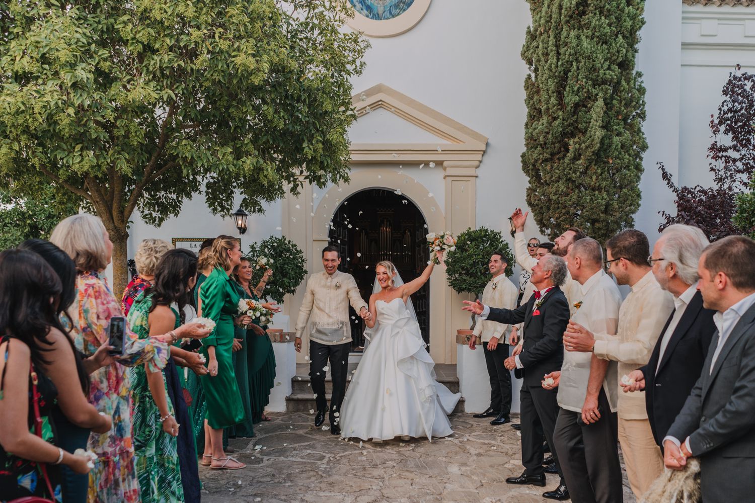 Wedding guests line a stone courtyard path outside a church during a celebratory exit.
