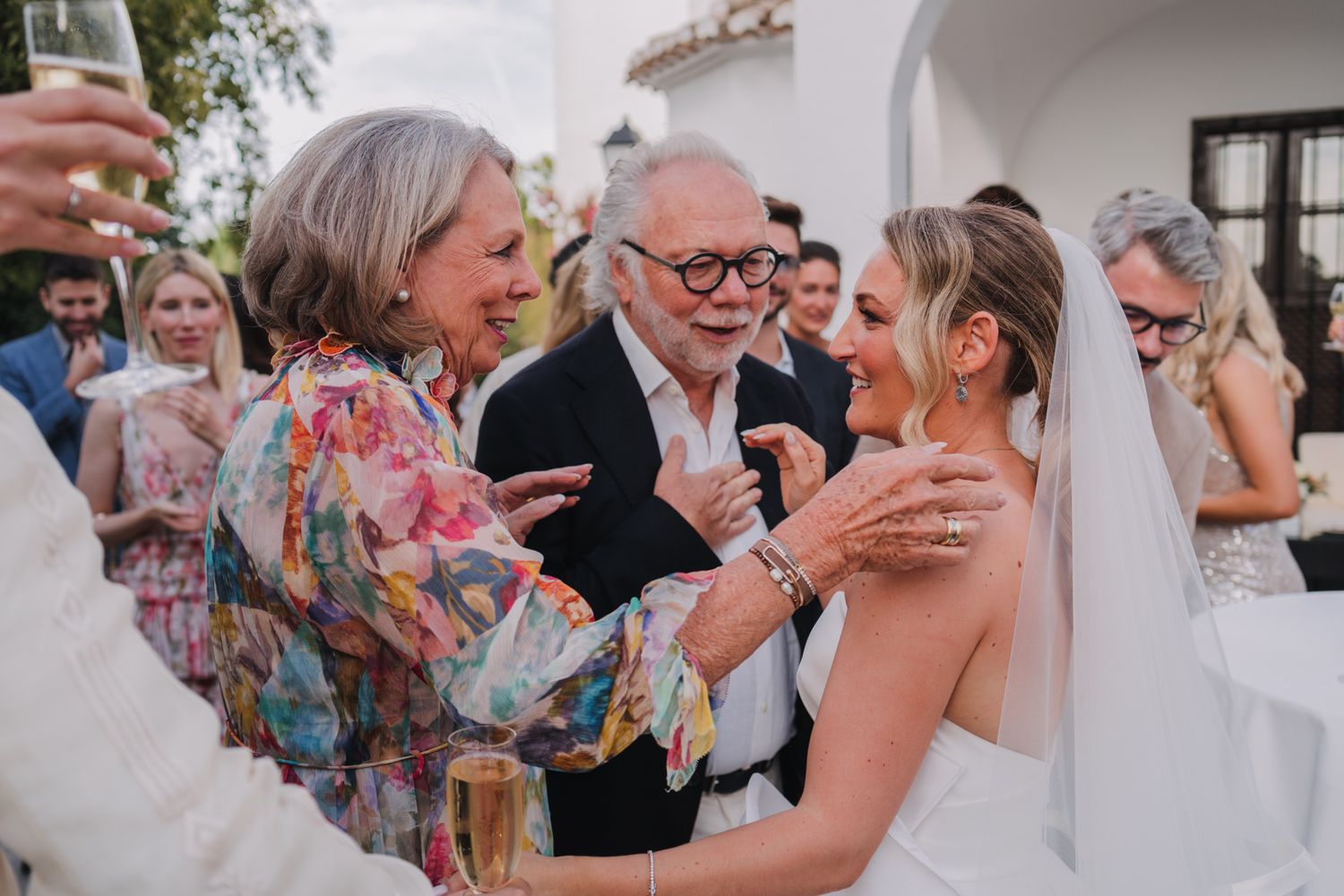 Celebratory moment during an outdoor wedding reception with guests interacting near white stucco walls.