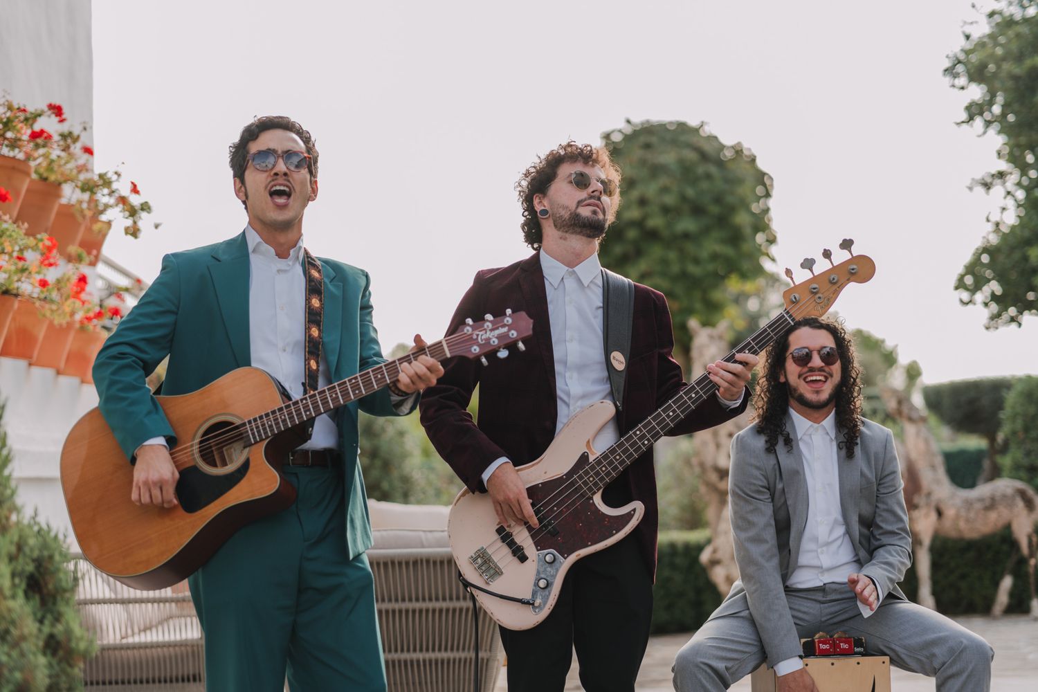 Three musicians performing outdoors with acoustic and electric guitars in formal attire during a wedding celebration.