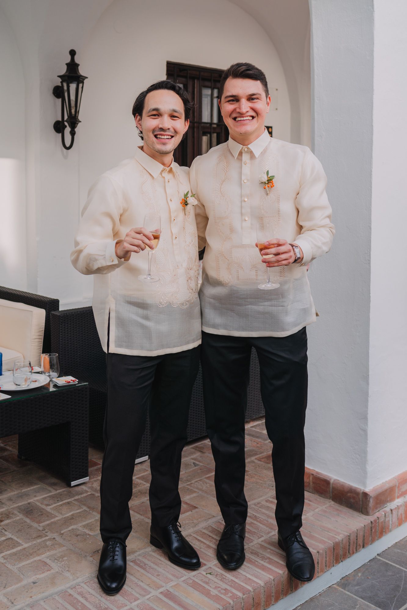 Two men in traditional Filipino barong tagalog formal wear pose with drinks at an event.