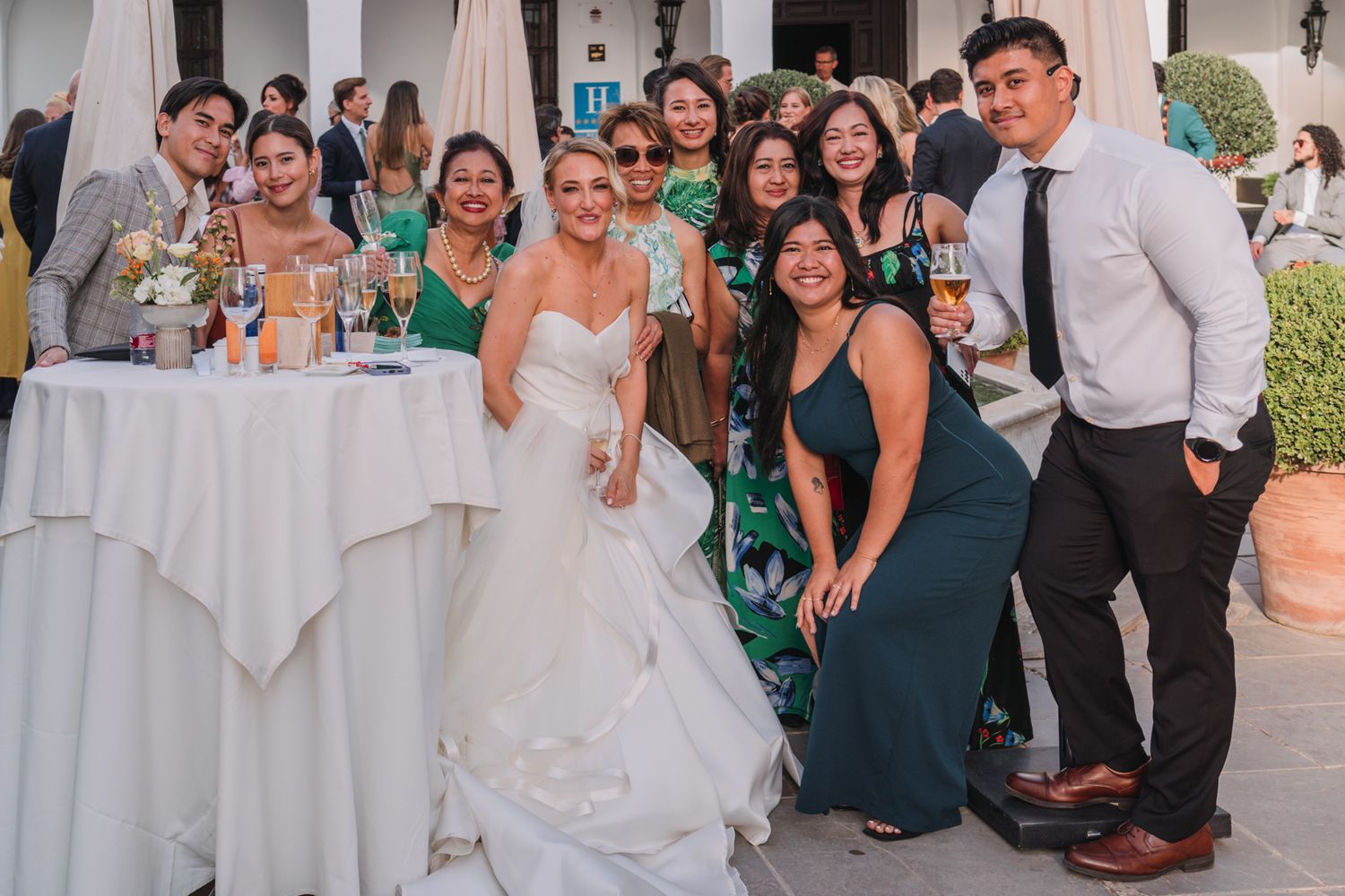 Wedding party guests pose for a group photo at an outdoor reception with tables and decor.