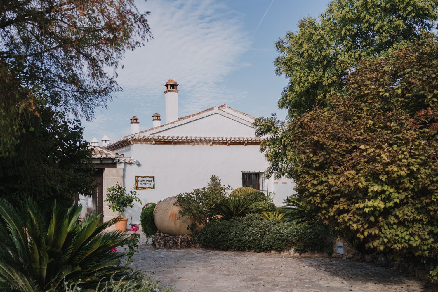 A white Spanish colonial style building with terracotta roof tiles amid lush garden landscaping.