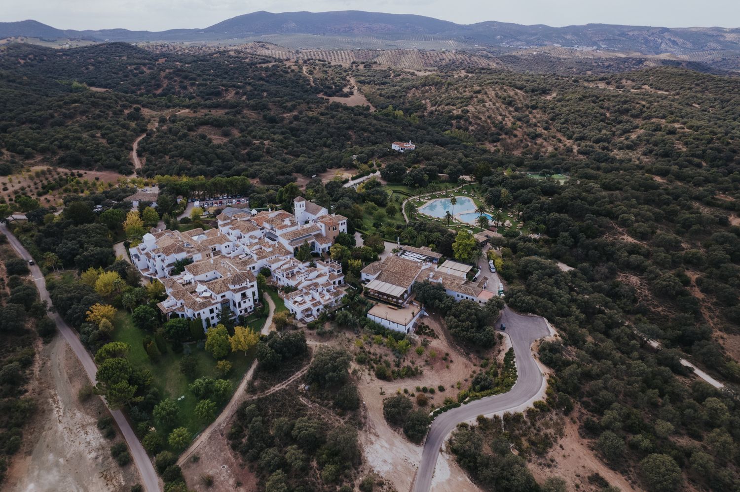 Aerial view of a white village nestled in mountainous terrain with winding roads and natural landscape.