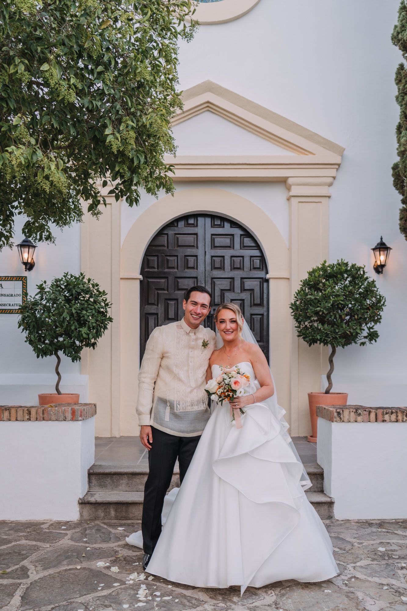 Wedding couple poses in front of an elegant arched doorway with Mediterranean architectural details.